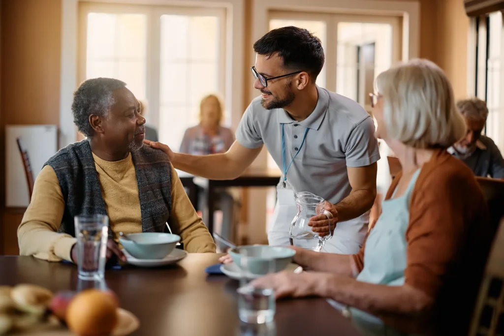 Seniors eating with caregiver delivering water